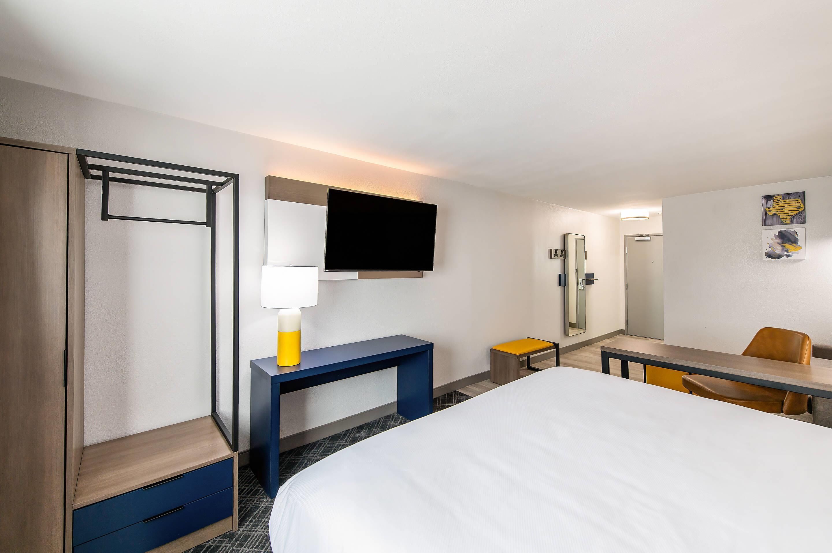 Habitación de hotel con cama, escritorio, silla, televisión, espejo y armario.