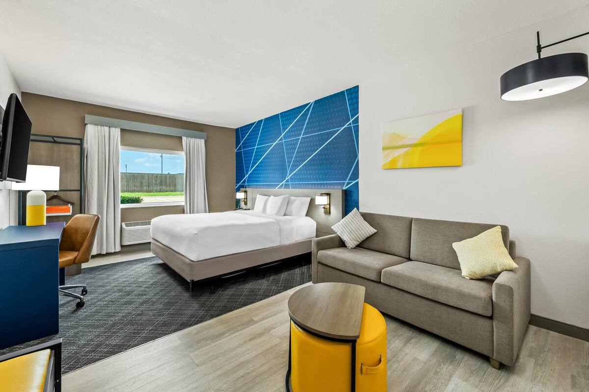 Quarto de hotel com cama, sofá, escrivaninha e televisão.