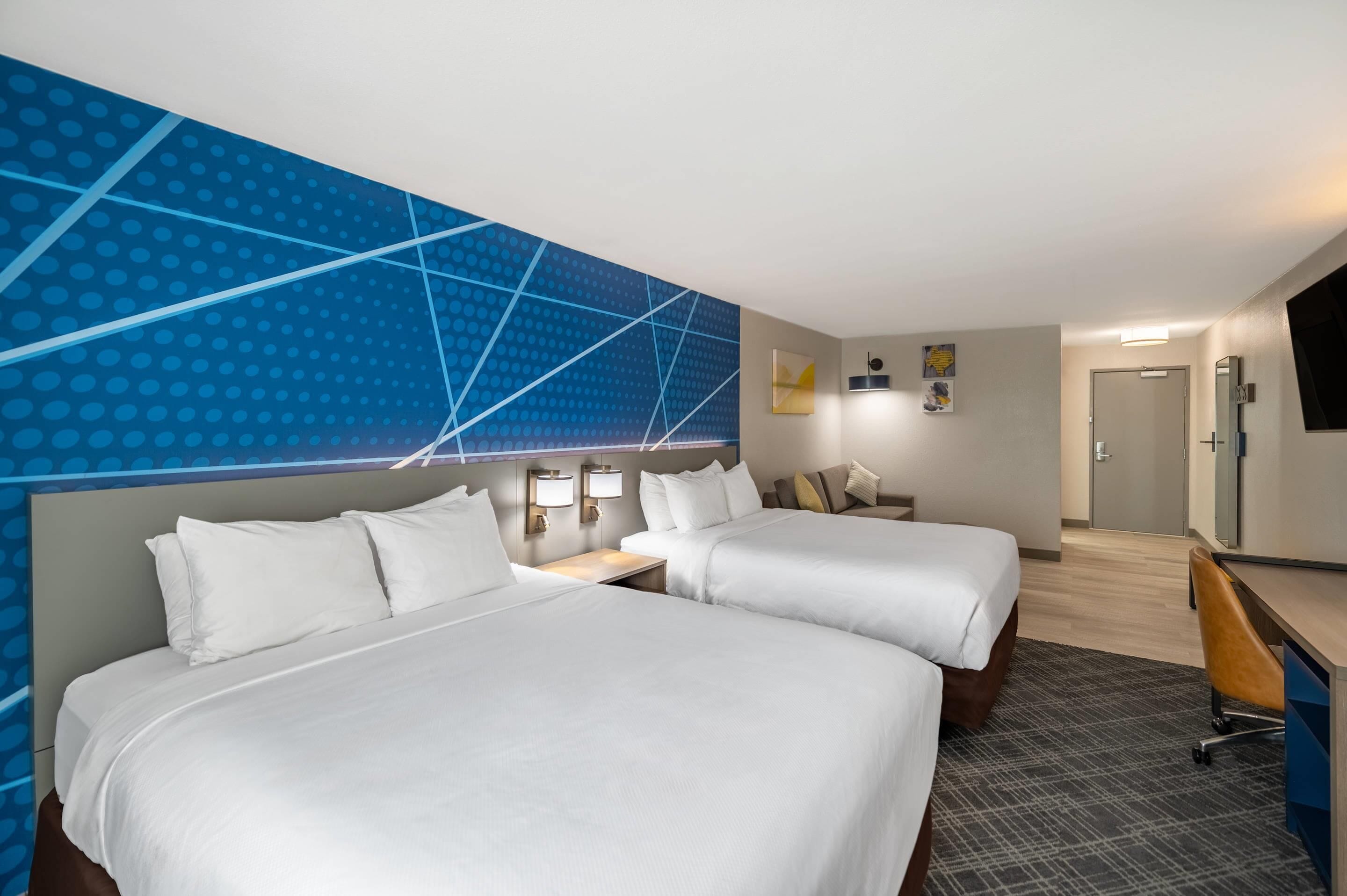 A hotel room with two beds, a desk, a chair, and a TV.