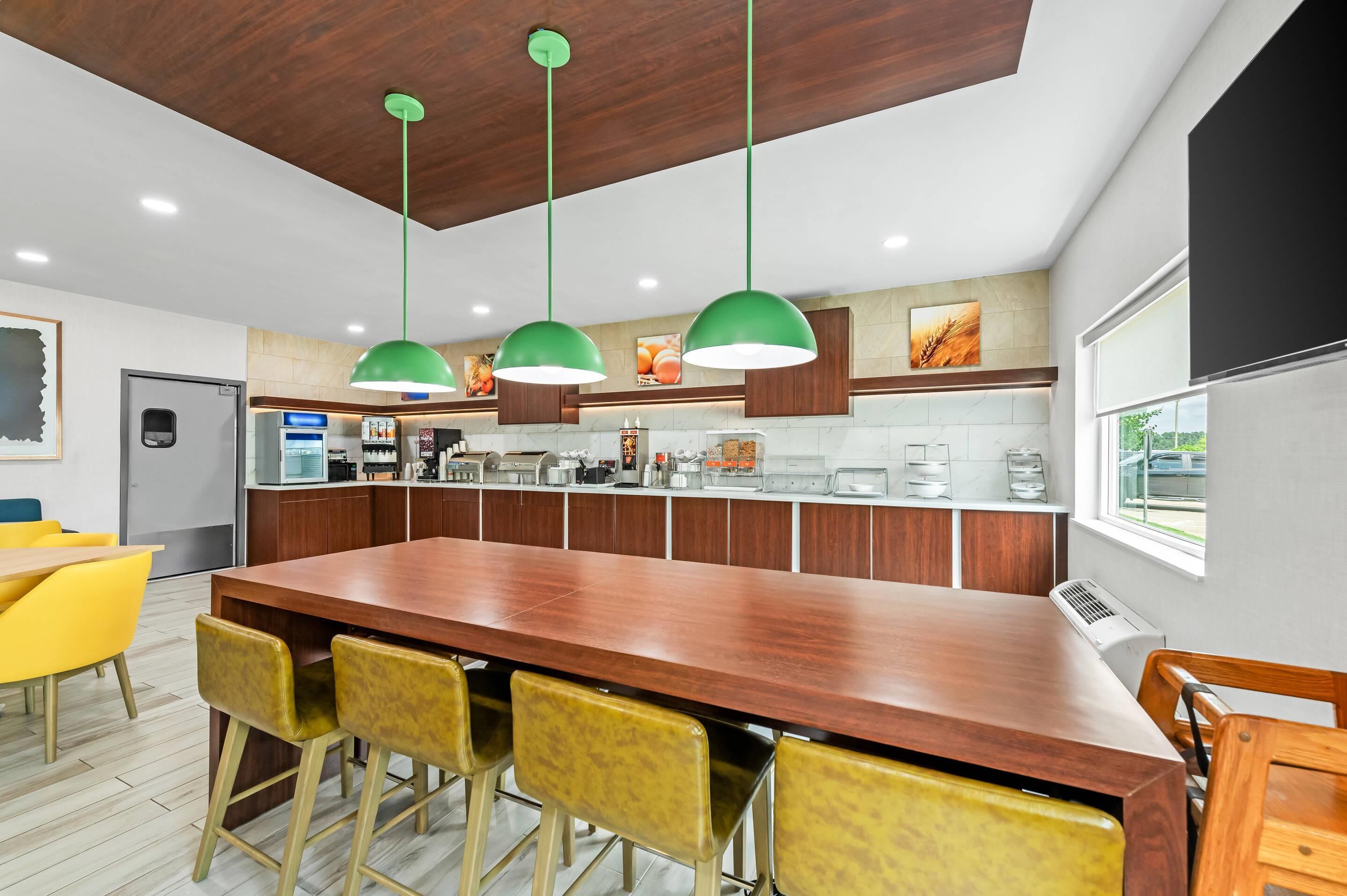 A modern kitchen with a central island, wooden cabinets, and green pendant lights.