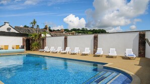 A swimming pool with lounge chairs and a white wall with brick accents. - Best Western Fowey Valley (Lostwithiel)