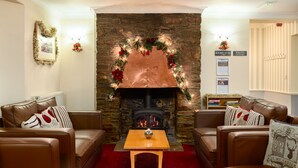A cozy living room with leather sofas, a wooden coffee table, and a stone fireplace adorned with Christmas decorations. - Best Western Fowey Valley (Lostwithiel)