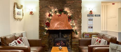 Una sala de estar acogedora con sofás de cuero, una mesa de centro de madera y una chimenea de piedra decorada con adornos navideños.