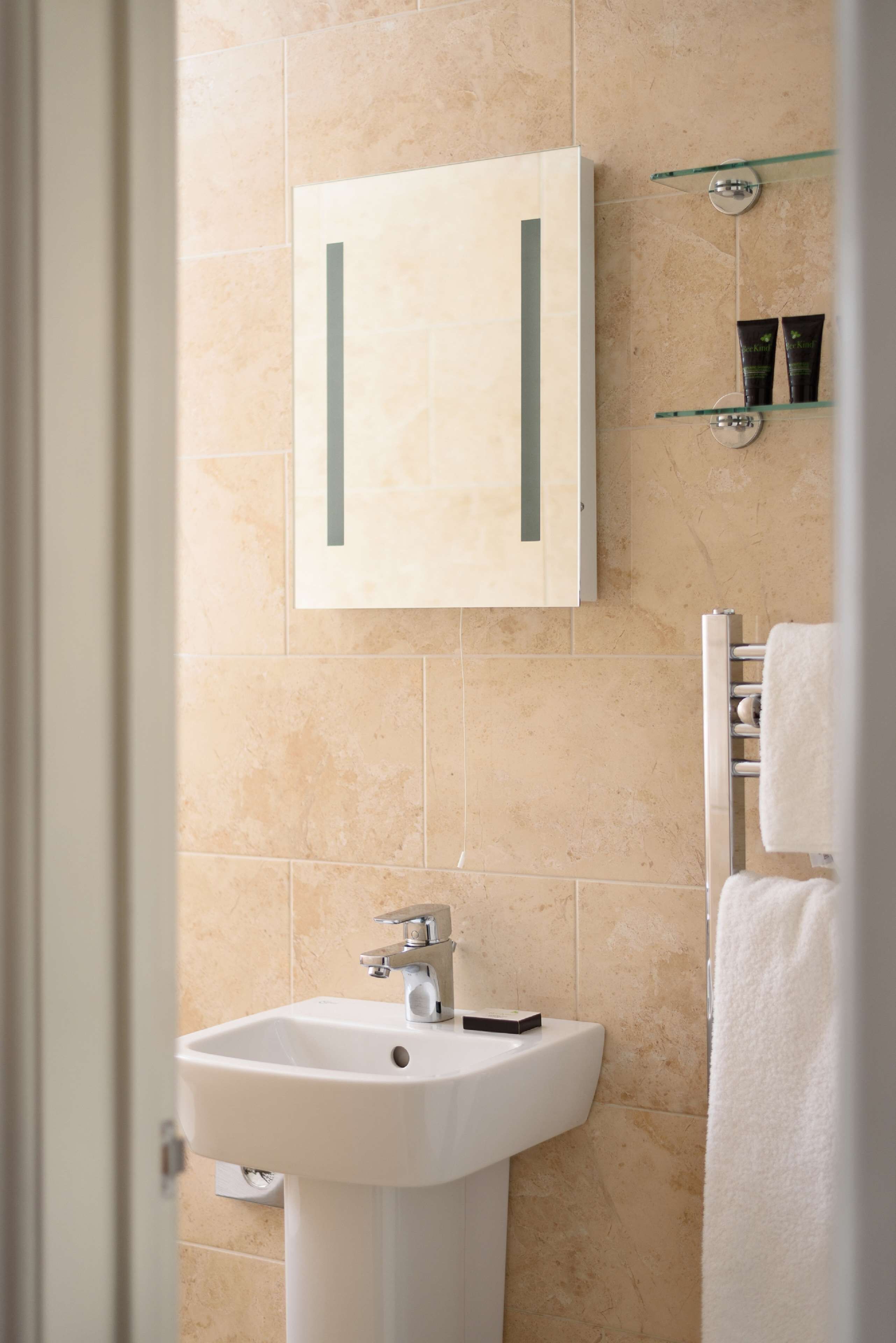 A bathroom with beige tiles, a white sink, a glass medicine cabinet, and a towel rack.