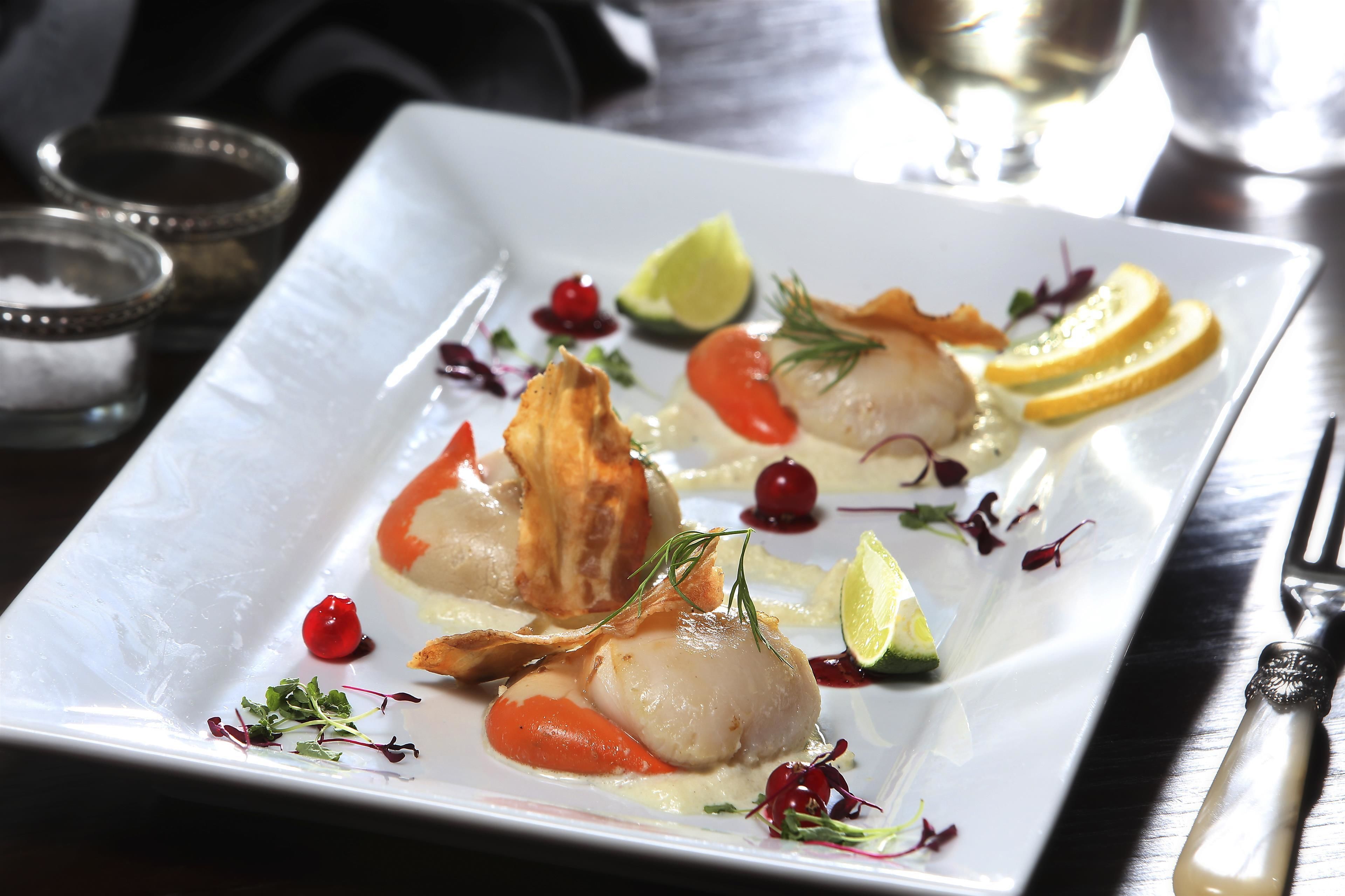 A square white plate with a seafood dish, garnished with herbs and citrus slices.