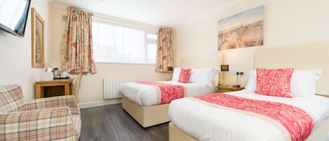 A hotel room with two beds, a sofa, a TV, a painting, and a window with curtains.