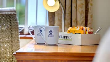 Uma mesa de madeira com duas canecas brancas identificadas com a marca Best Western, uma caixa de snacks Clipper e um abajur.