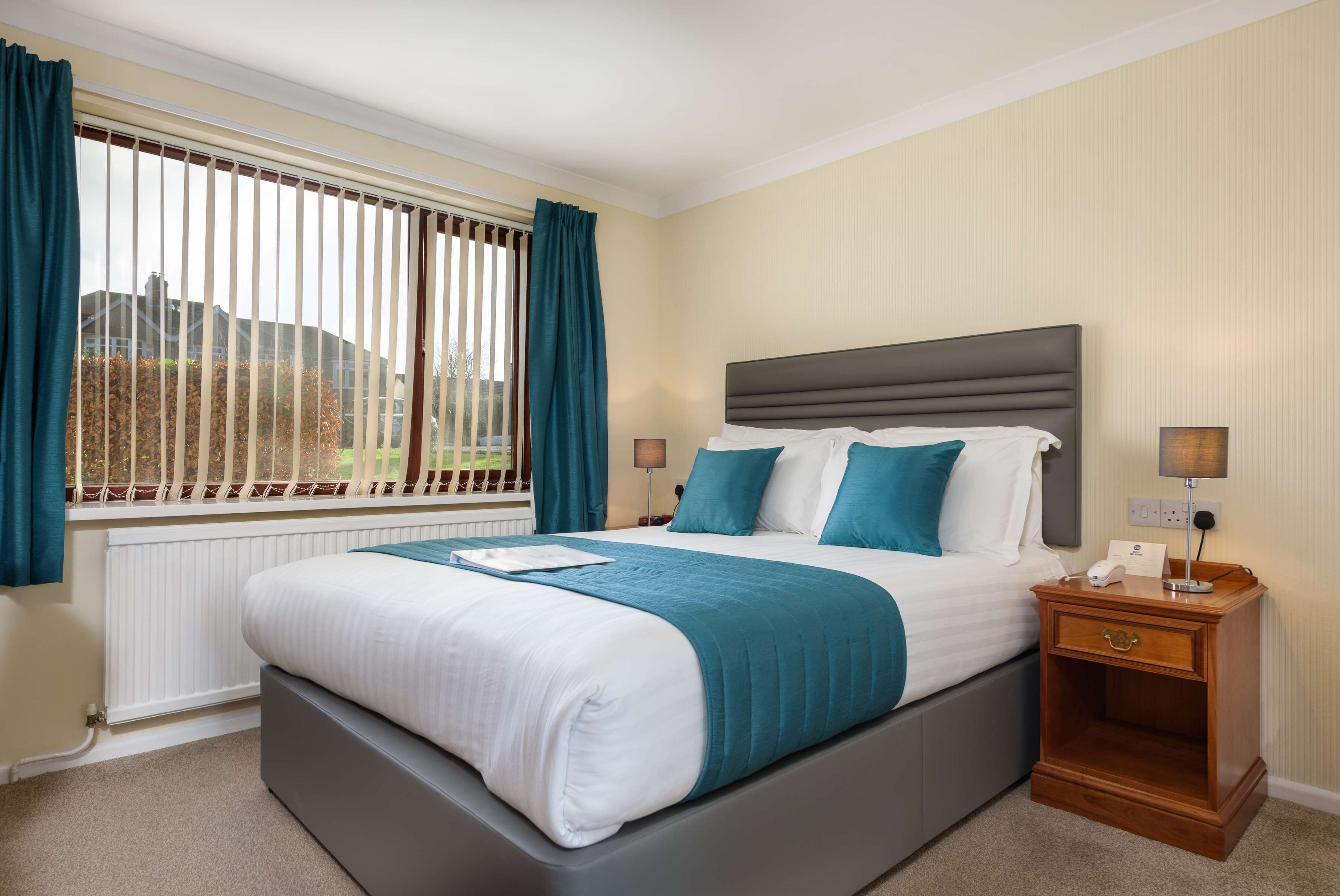 A bedroom with a large bed, a nightstand, a window with curtains, and a view of the outside.