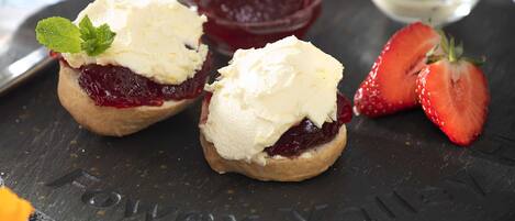 Three scones with cream and jam, a strawberry, and a bowl of jam on a slate board.