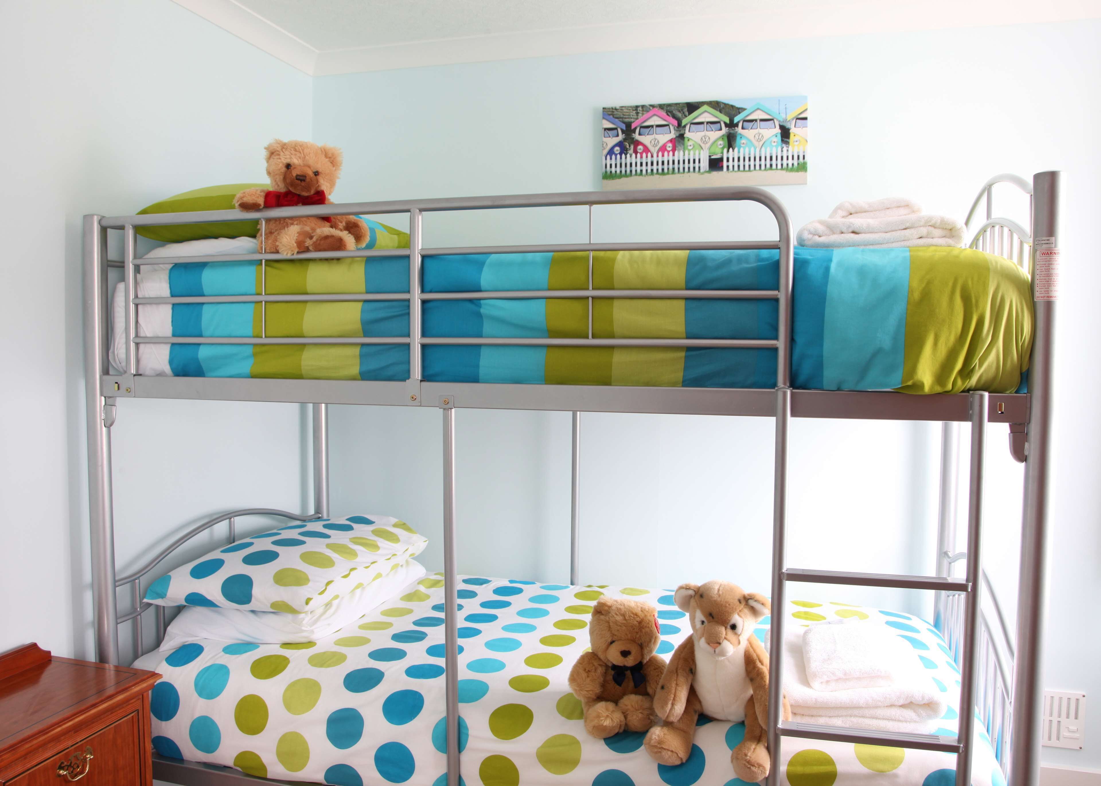 A bunk bed with a teddy bear on the top bunk and another on the bottom.