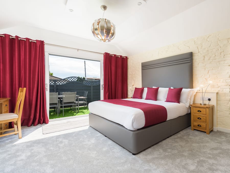 A bedroom with a large bed, a nightstand, a lamp, and a view of the outside.