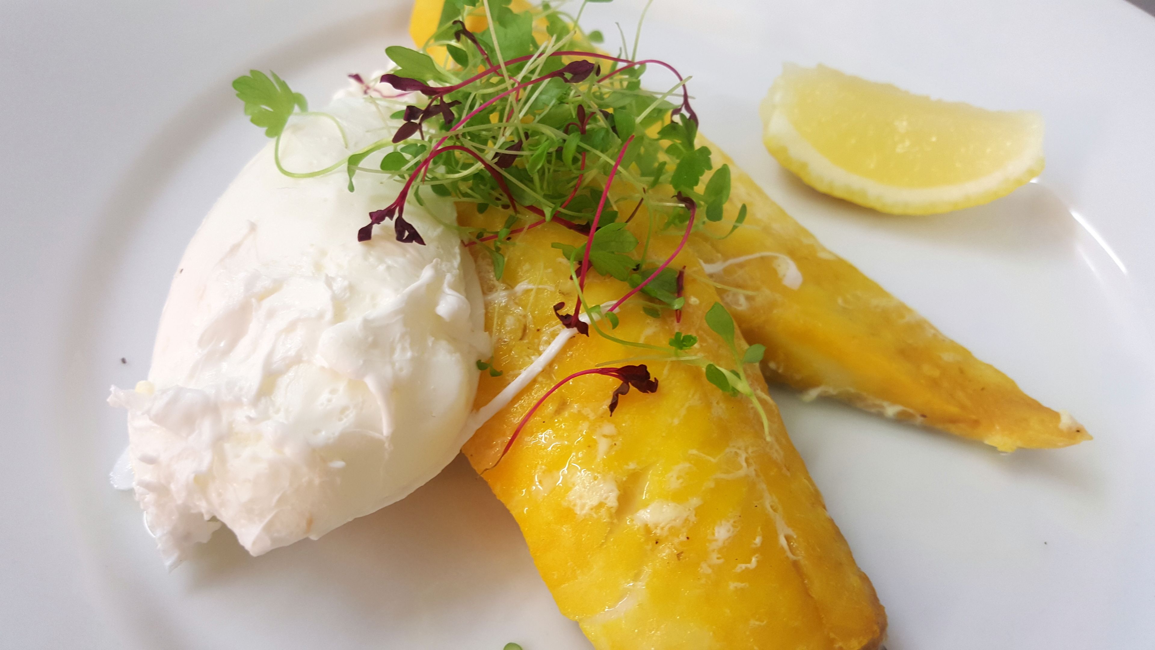 A plate with a piece of white fish, a slice of lemon, and a wedge of mango.