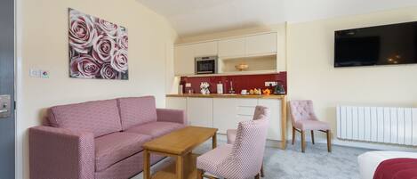 Een compacte leefruimte met een kitchenette, een bank, een eettafel en een aan de muur bevestigde televisie.