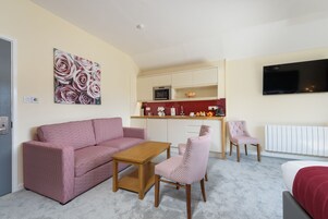 Un espacio habitable compacto con kitchenette, un sofá, una mesa de comedor y un televisor instalado en la pared.