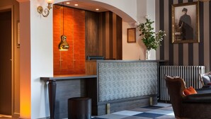 Ein Empfangsbereich mit einer Rezeption, einer großen Vase mit Blumen, einem gerahmten Foto an der Wand und einer Wandverkleidung mit Muster.