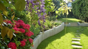 Ein gepflegter Garten mit geschwungenem Steinrand, üppigem Grün und leuchtenden Blumen.