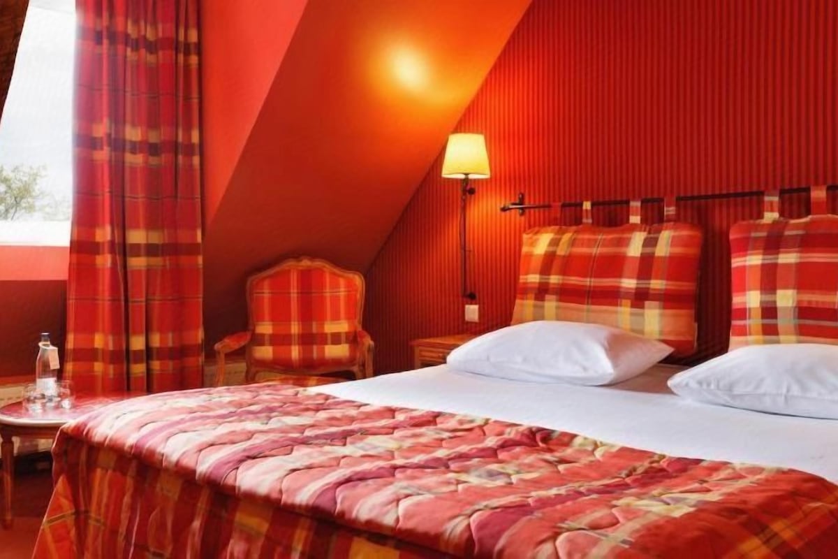 A hotel room with a large bed, a chair, a table with a bottle, and a lamp.