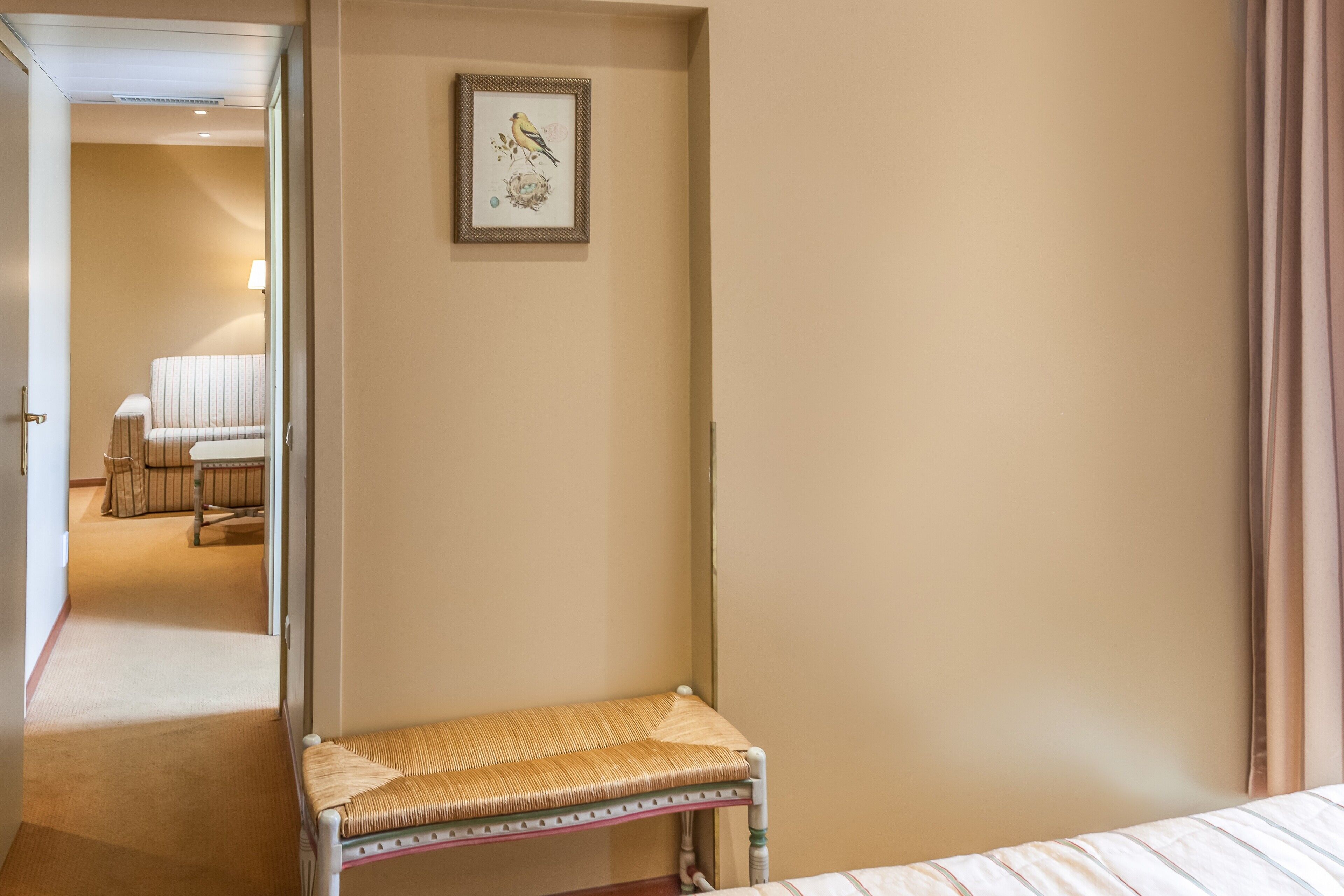 Una camera d'albergo con un letto, una piccola panca, un quadro appeso alla parete e un'occhiata fugace al bagno sullo sfondo.