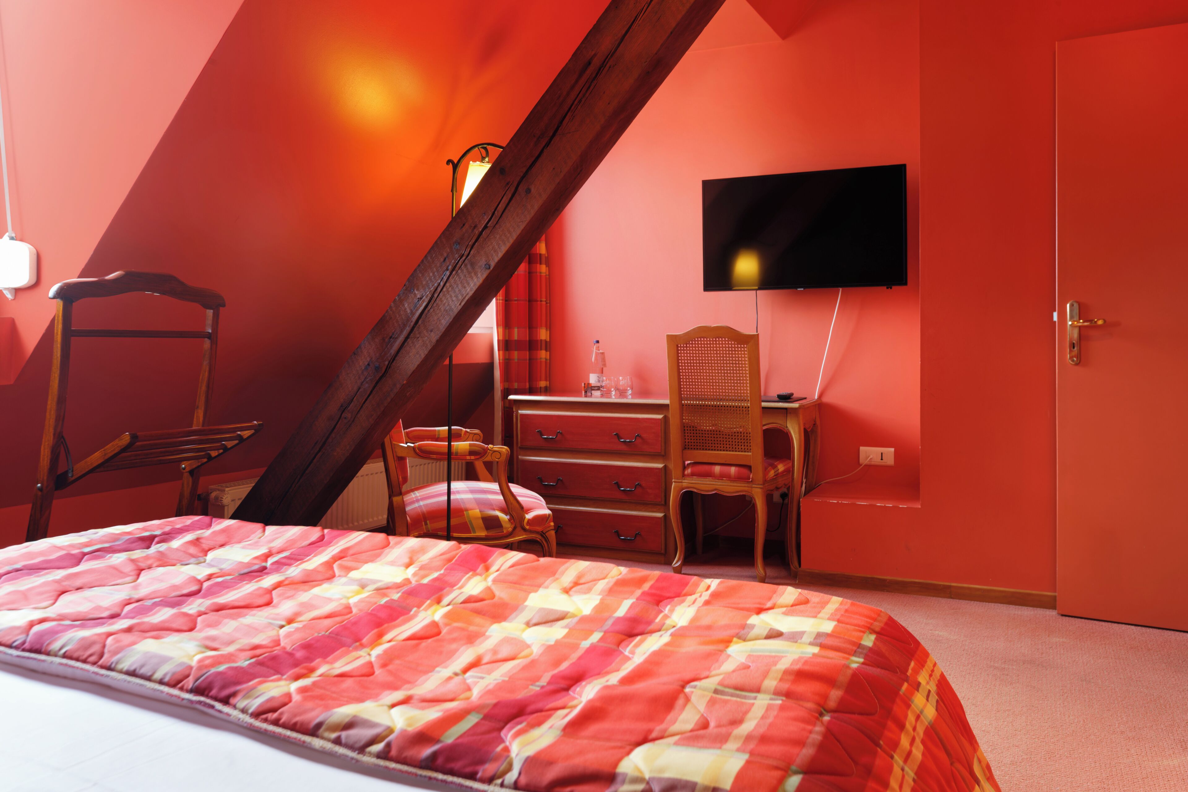A bedroom with a bed, a desk, a chair, a television, and a door.