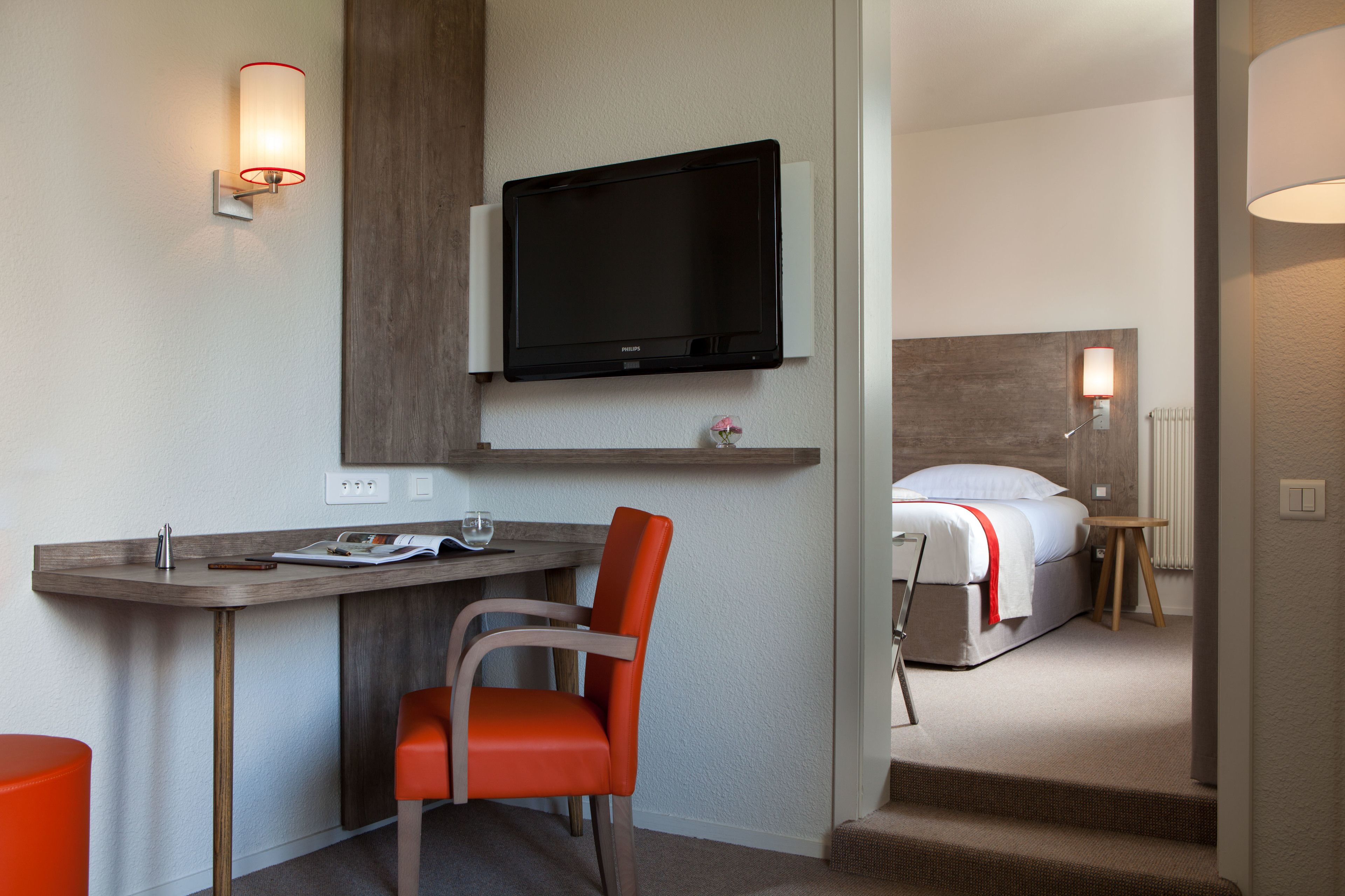 Een hotelkamer met een bureau, stoel, televisie, bed en een kleine tafel met een lamp.