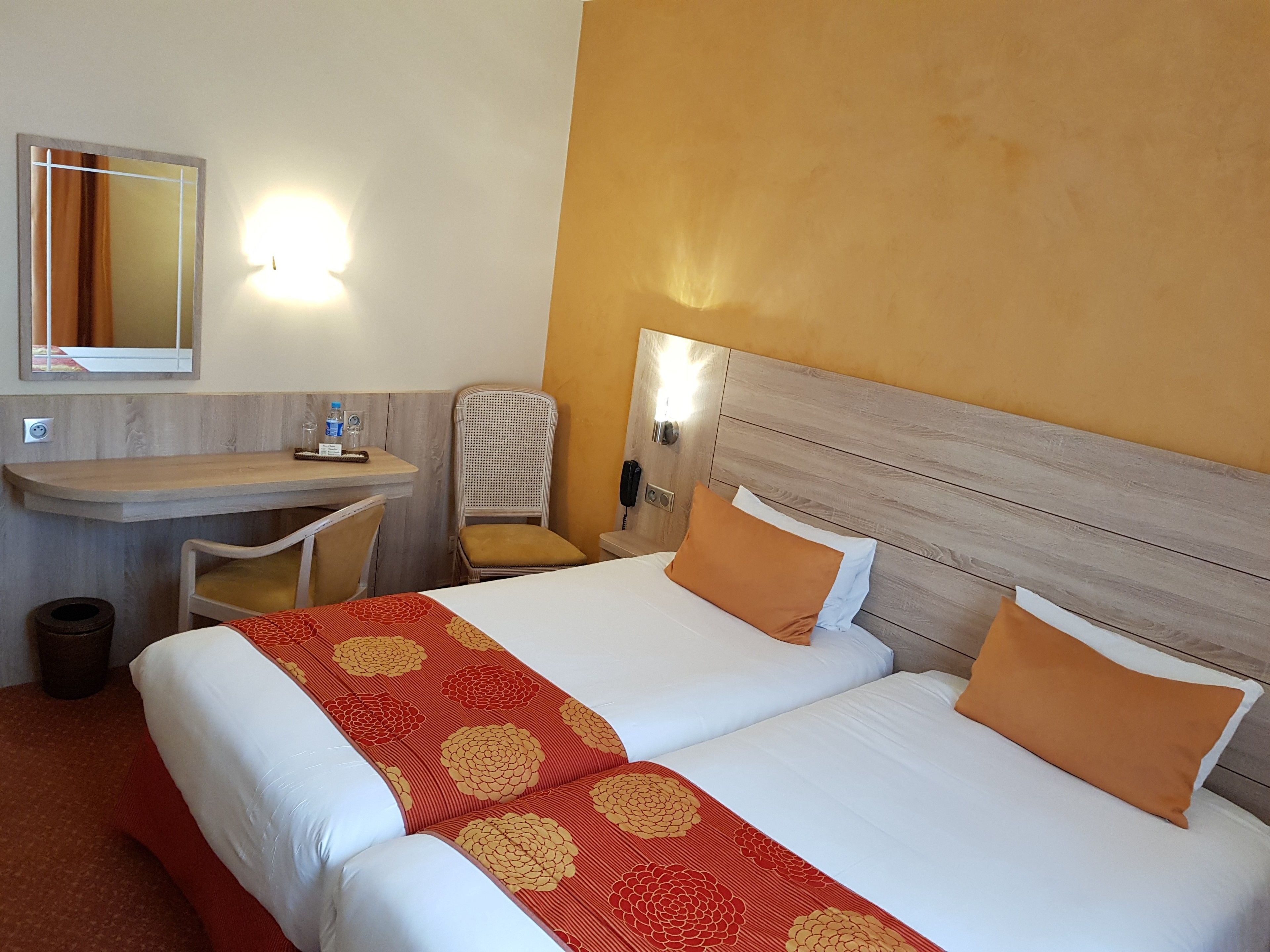 A hotel room with two beds, a desk, a chair, a trash bin, and a wall-mounted phone.