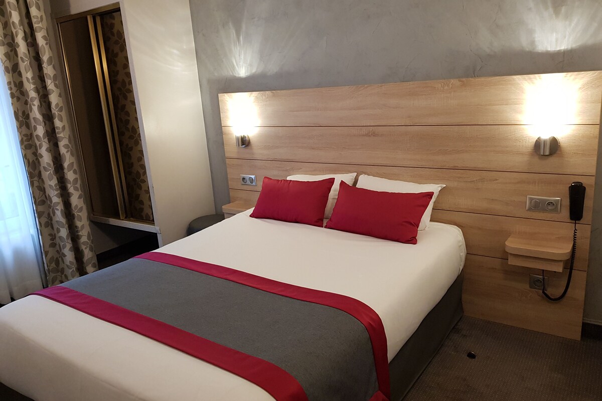 A hotel room with a bed, a bedside table, a phone, and a wall-mounted light.