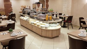 A breakfast buffet area with various food items and beverages, surrounded by tables and chairs. - Hotel Champerret Elysees (Paris)