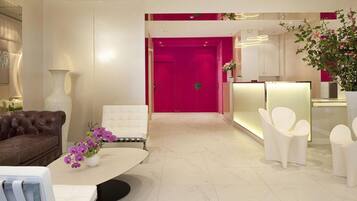 A modern lobby with a leather sofa, a white armchair, a reception desk, and a large vase with purple flowers.