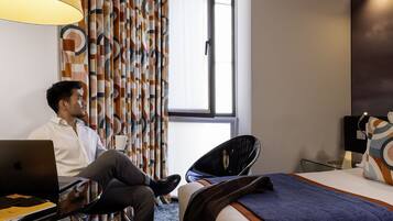 Een hotelkamer met een bed, een bureau met een laptop en een raam met gordijnen.