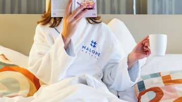 Une personne est assise dans une chambre d’hôtel, un livre à la main, devant un lit, des oreillers et un téléviseur fixé au mur.
