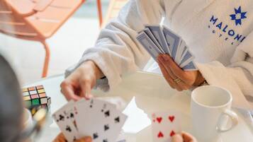 A person in a white robe playing cards at a table with a Rubik's cube and a white mug.
