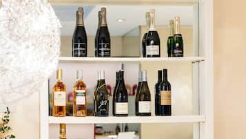 Un coin bar avec des étagères remplies de bouteilles de différentes sortes d’alcool, un verre décoratif et deux verres contenant une boisson dorée.
