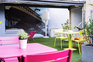 A patio area with a pink table and chairs, a yellow table with chairs, and a white lamp. There is a mural of a bridge on the wall.