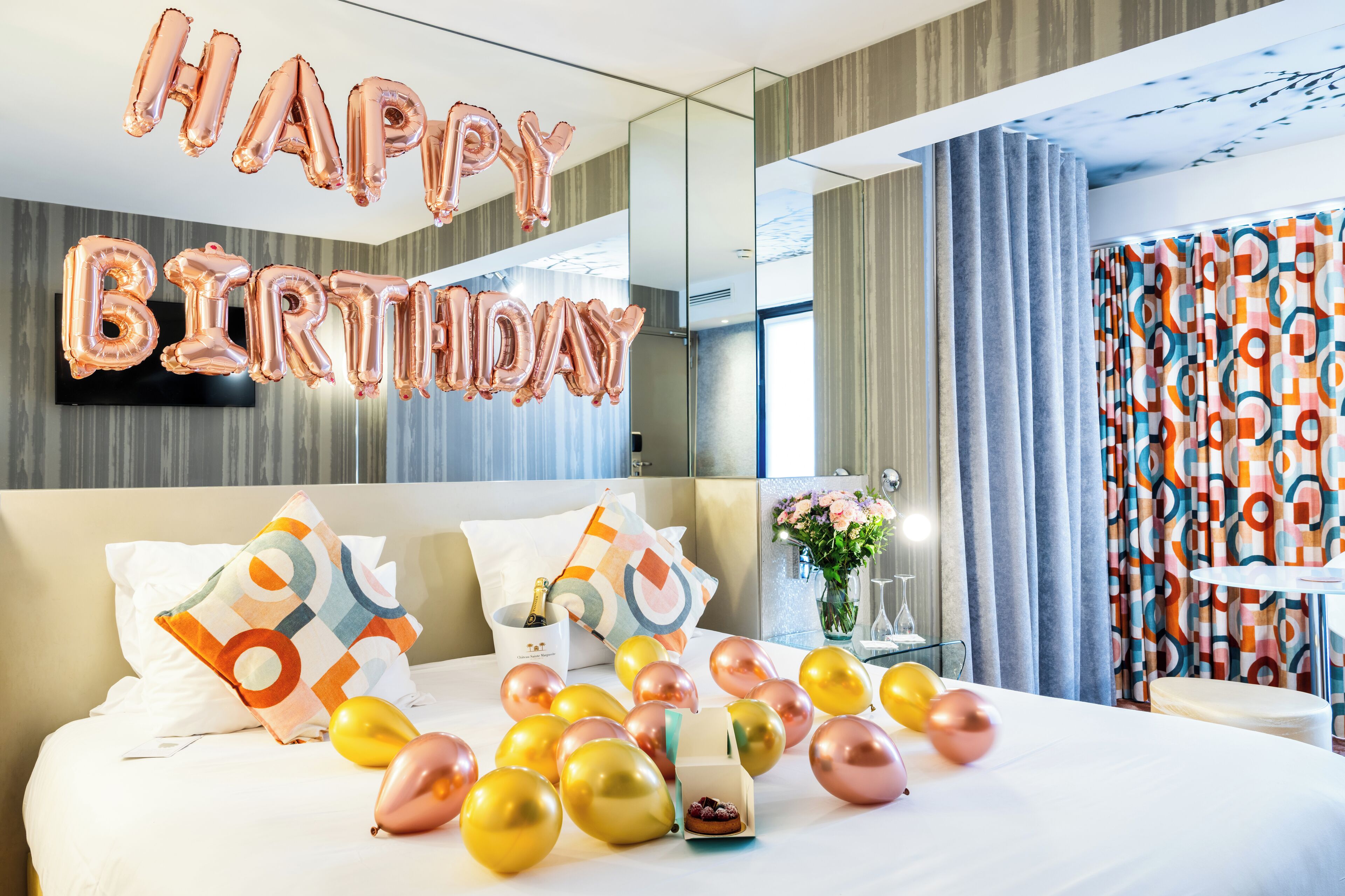 Ein Hotelzimmer mit einem Bett, Kissen, einem Nachttisch mit Blumen und einem großen Fenster mit Vorhängen.