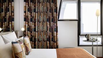 Une chambre d’hôtel comprenant un lit, des oreillers, une fenêtre avec des rideaux, une table de chevet avec une lampe et une machine à café.