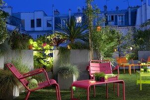Un patio con sedie rosse e un tavolo, circondato da piante in vaso e un piccolo giardino.