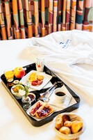 A breakfast tray with various foods and drinks on a bed with a white sheet and a white pillow.