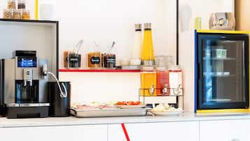 A breakfast bar with a coffee machine, juice dispensers, and a refrigerator.