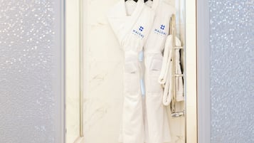 A bathroom with a glass door, marble walls, and white towels hanging on a rack.