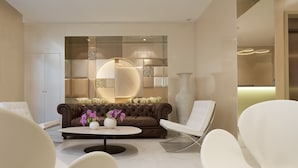 Een moderne woonkamer met een bruine leren bank, witte stoelen, een bijzettafeltje met bloemen en een grote vaas.