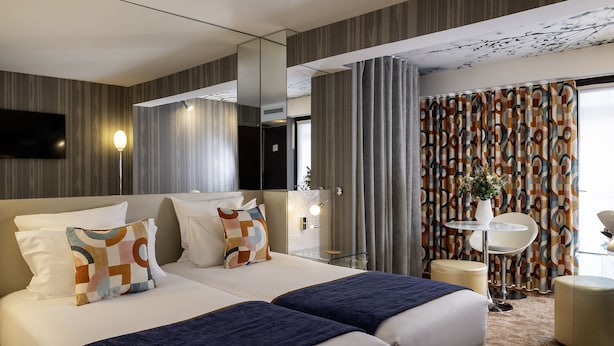 Een hotelkamer met een groot bed, twee nachtkastjes, een televisie en uitzicht door gordijnen.