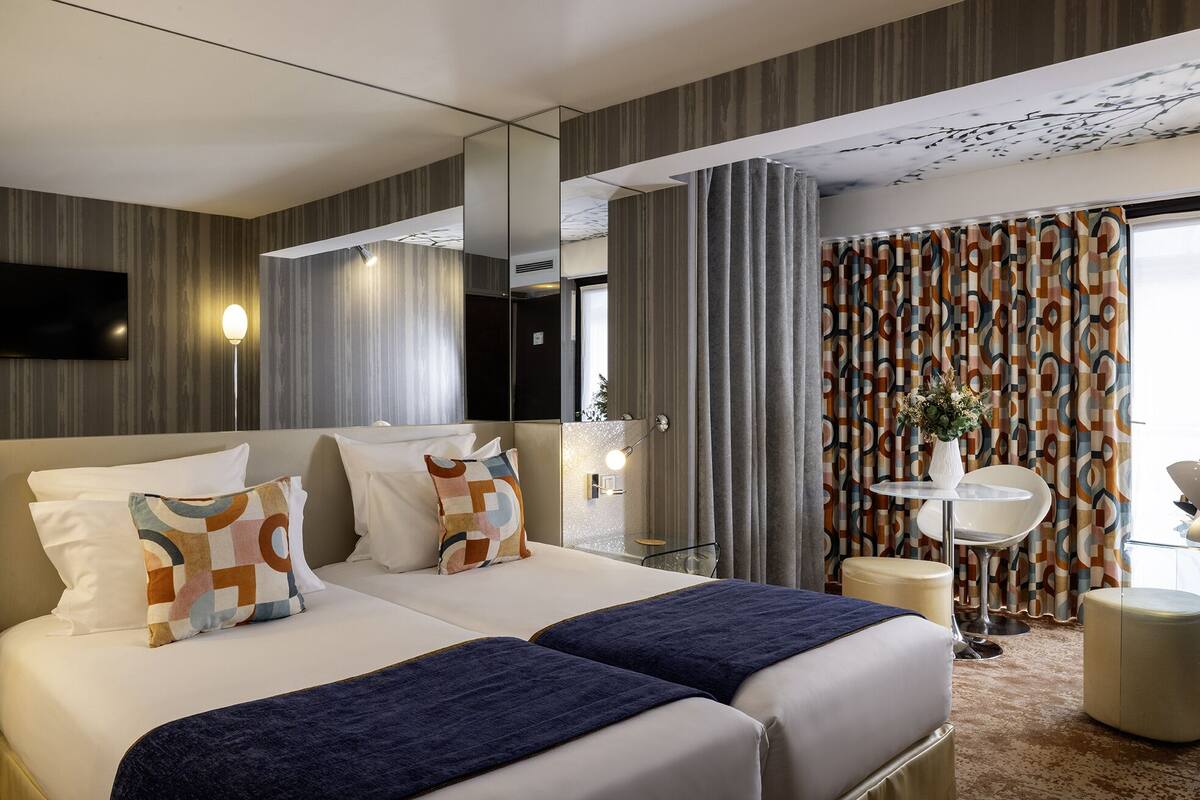 A hotel room with a large bed, two bedside tables, a TV, and a view of the outside through curtains.