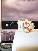 A hotel room with a bed, a round table, and a wall-mounted light fixture.
