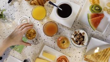 Desayuno con cruasanes, panqueques, fruta y diferentes mermeladas sobre una mesa con textura.
