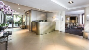 A modern hotel lobby with a reception desk, seating area, and a dining space. - Hotel Elysées Flaubert (Paris)
