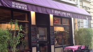 A restaurant with a purple awning, outdoor seating with red and white checkered tables, and a menu board visible through the window. - Hotel Elysées Flaubert (Paris)