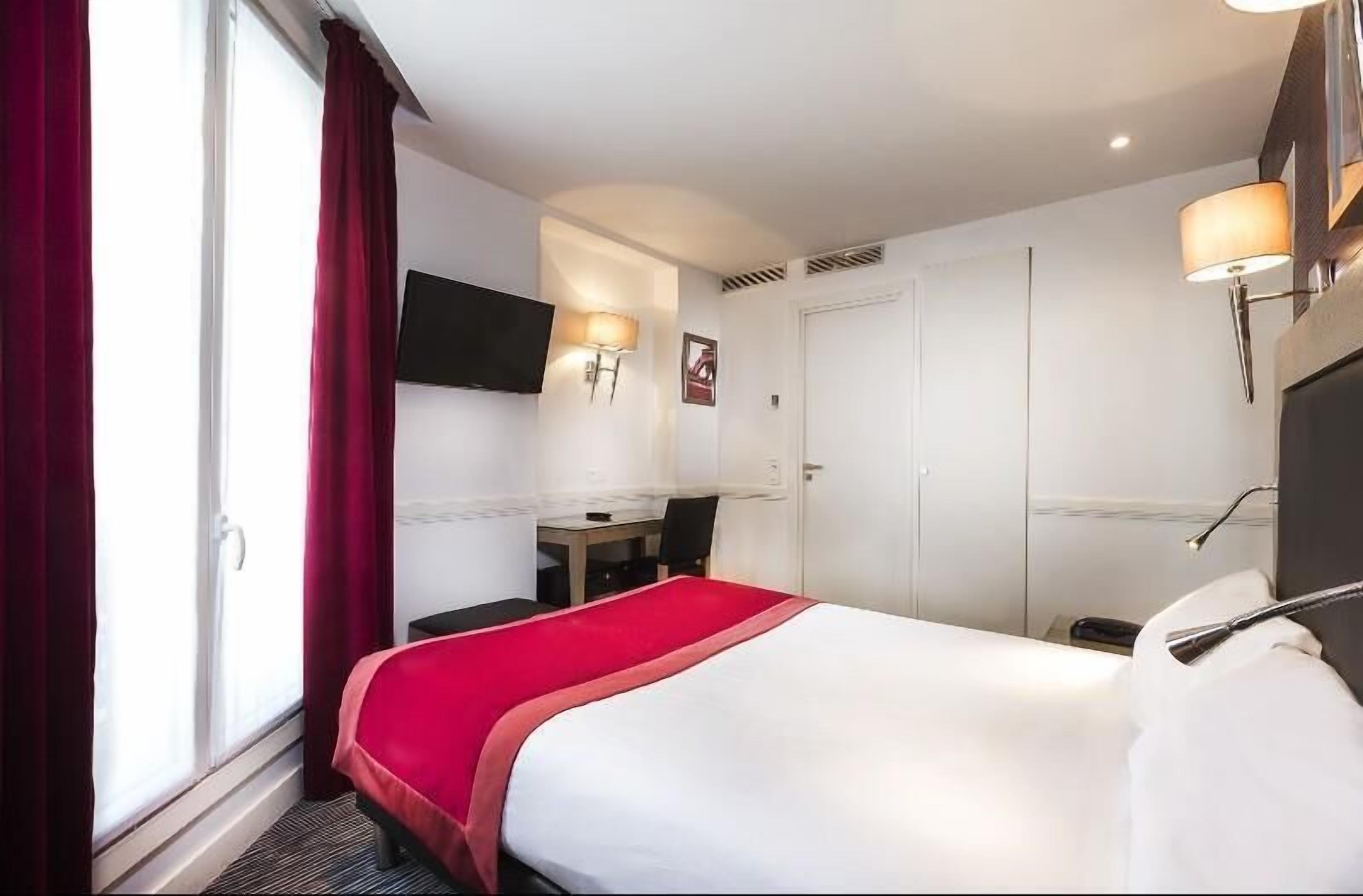 Una habitación de hotel con cama, escritorio, silla, televisor y armario.