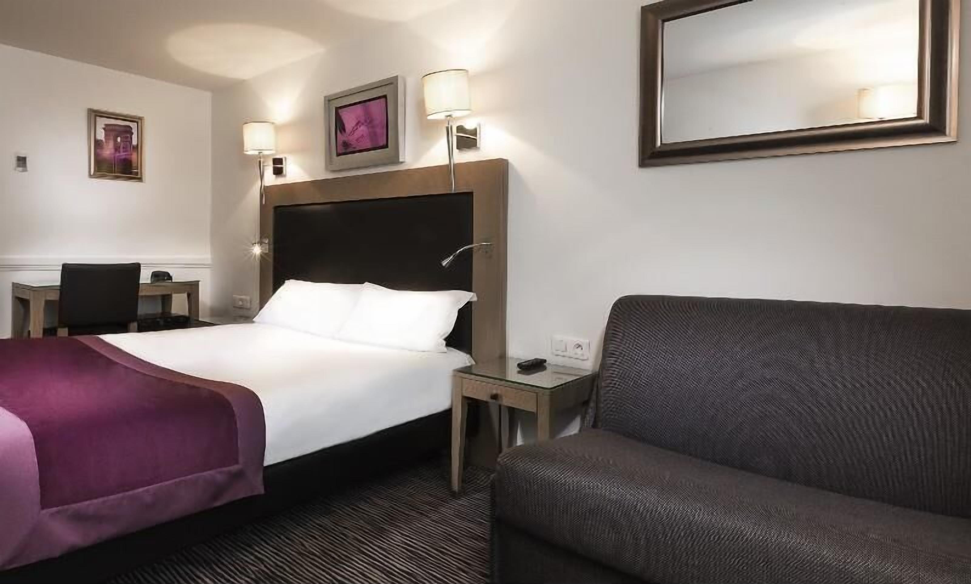 Ein Hotelzimmer mit Bett, Sessel, Schreibtisch und Spiegel.