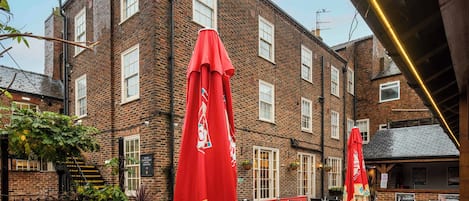 A brick building with outdoor seating, a staircase, and a red umbrella.