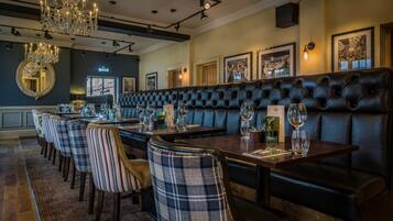A restaurant with a long counter, upholstered booths, and a chandelier.